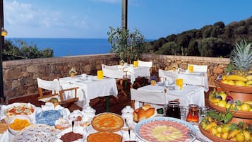 Zona pranzo all'aperto con tavoli apparecchiati per la colazione, con vista sul mare.