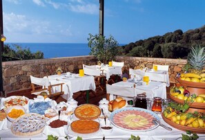 Uma área de refeições ao ar livre com mesas preparadas para o café da manhã, com vista para o mar.