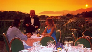 Ein Tisch ist für eine Mahlzeit gedeckt, mit Blick auf den Sonnenuntergang und die Berge im Hintergrund.