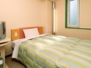 Ein Einzelbett mit gestreifter Bettdecke, ein Nachttisch mit Lampe und ein Fenster mit grünem Rahmen.
