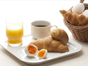 Bandeja de desayuno con un croissant, un huevo duro a medio comer, un vaso de jugo de naranja y una taza de café.