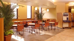 A hotel dining area with round tables and orange chairs, potted plants, and a water fountain. - R&B Hotel Sendai-hirosedoriekimae (Sendai)
