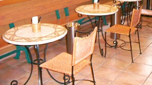 A row of round tables with chairs, each with a patterned tabletop and metal legs, in a tiled room with a wooden accent wall. - R&B Hotel Sendai-hirosedoriekimae (Sendai)