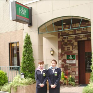 Two individuals standing in front of a hotel entrance with a signboard. - R&B Hotel Sendai-hirosedoriekimae (Sendai)