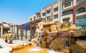 Un hotel con una fuente de agua, plantas en macetas y un cielo azul despejado.