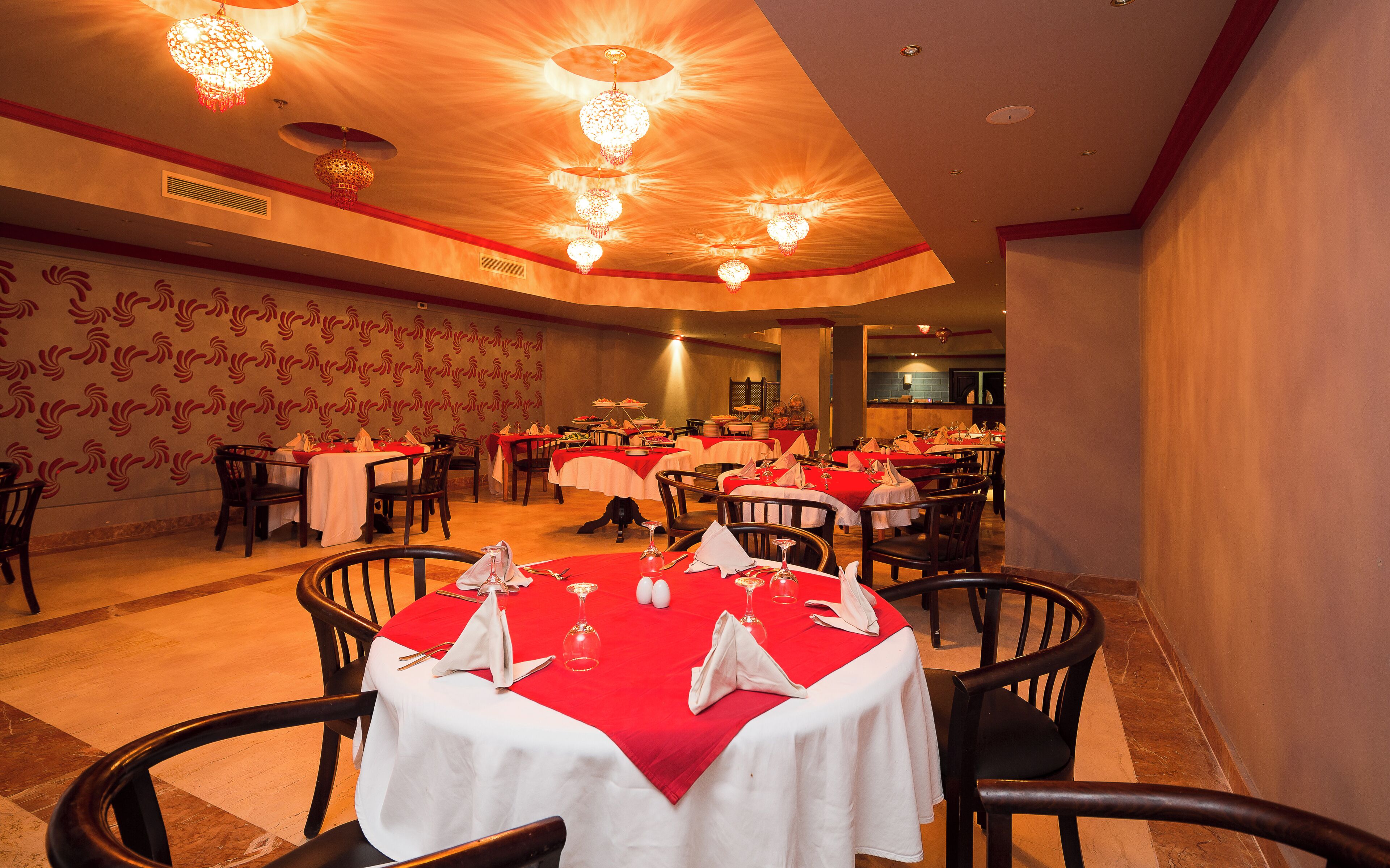 Une salle de banquet avec des tables rondes, des chaises et un mur orné de motifs.