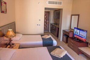 Habitación de hotel con dos camas, televisión, escritorio y baño visible a través de una puerta abierta.