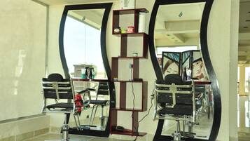 Un salón con dos sillones de barbero con espejo, un estante con productos para el cabello y un espejo grande que refleja el espacio.