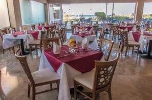 Un restaurant avec des tables dressées pour le service, des chaises et une vue sur la mer.