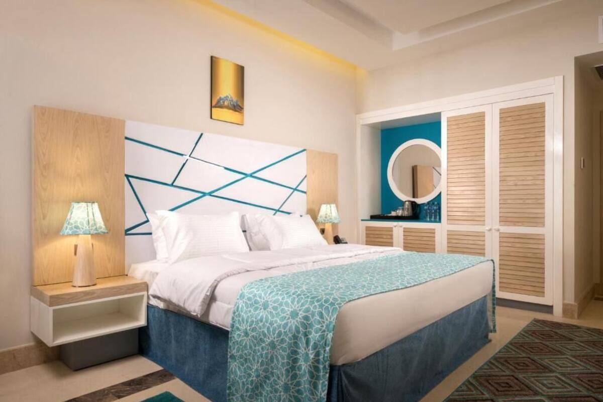 Un dormitorio con cama, lámparas de noche, cabecera con diseños geométricos, mesita de noche, una obra de arte colgada en la pared, un espejo circular y un armario con puertas correderas.