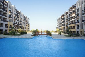 Une piscine offrant une vue dégagée sur un immeuble doté de nombreux balcons et d’une arche centrale.
