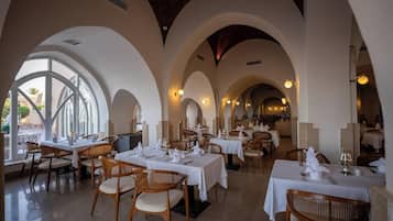 Un restaurante con varias mesas y sillas, techos abovedados y ventanas amplias.