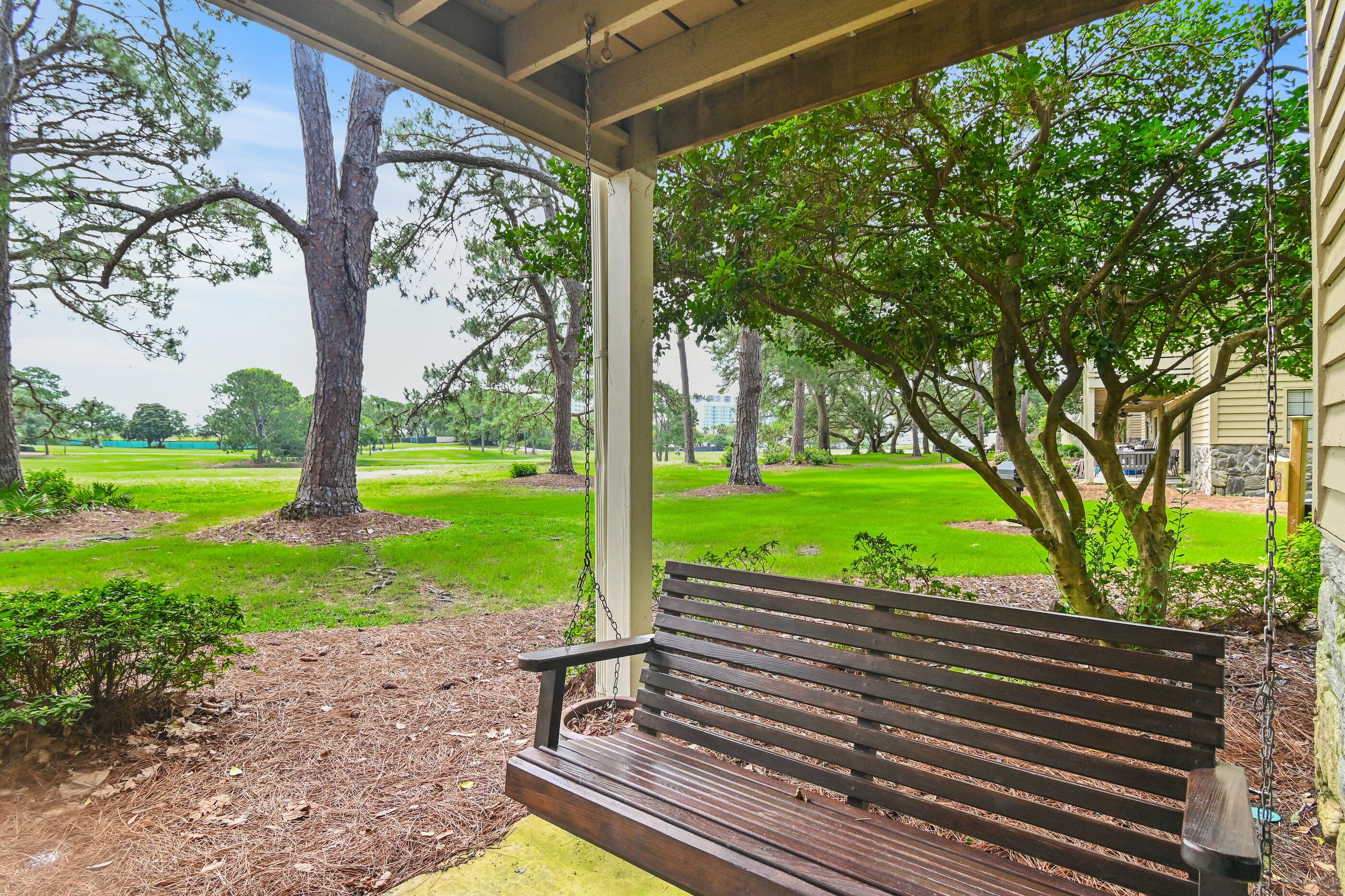 A wooden bench under a covered area with a view of a park and trees.