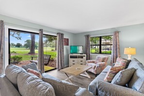 A living room with a sofa, armchair, TV, and a table. - ☀️Ground Floor | Golf Cart | Walk to Beach | Seascape 10E⛱️ (Miramar Beach)