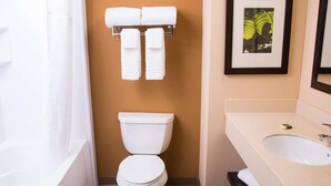 Ein Badezimmer mit Toilette, Waschbecken und Dusche. Handtücher hängen an einem Ablagekorb über der Toilette.