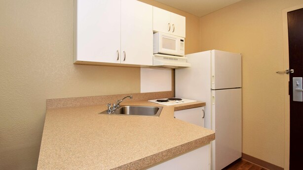 A kitchen with white cabinets, a microwave, a sink, and a refrigerator. - Extended Stay America - Fort Wayne - South (Fort Wayne)