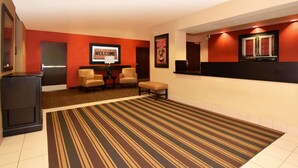 Eine Hotellobby mit Streifenmuster-Teppich, einer Rezeption, zwei Stühlen und einem 'Welcome'-Schild.
