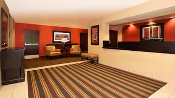A hotel lobby with a striped carpet, a reception desk, two chairs, and a 'Welcome' sign.