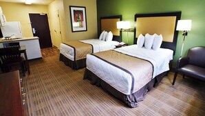 Ein Hotelzimmer mit zwei Betten, einem Schreibtisch, einem Stuhl und einer Küchenzeile.