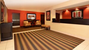 A hotel lobby with a striped carpet, a reception desk, two chairs, and a 'Welcome' sign. - Extended Stay America - Fort Wayne - South (Fort Wayne)