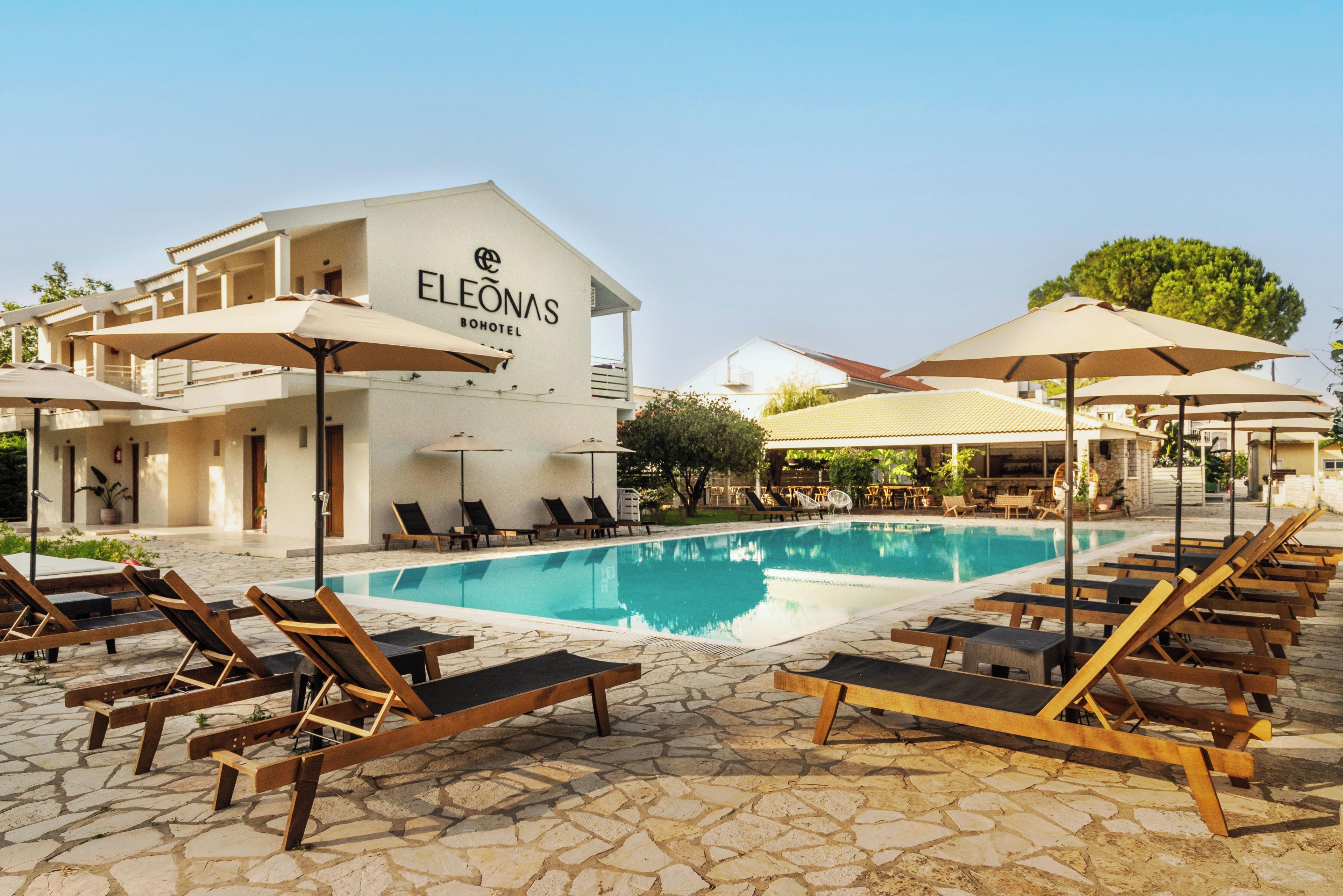 A hotel named ELEONAS with a swimming pool, lounge chairs, and umbrellas.