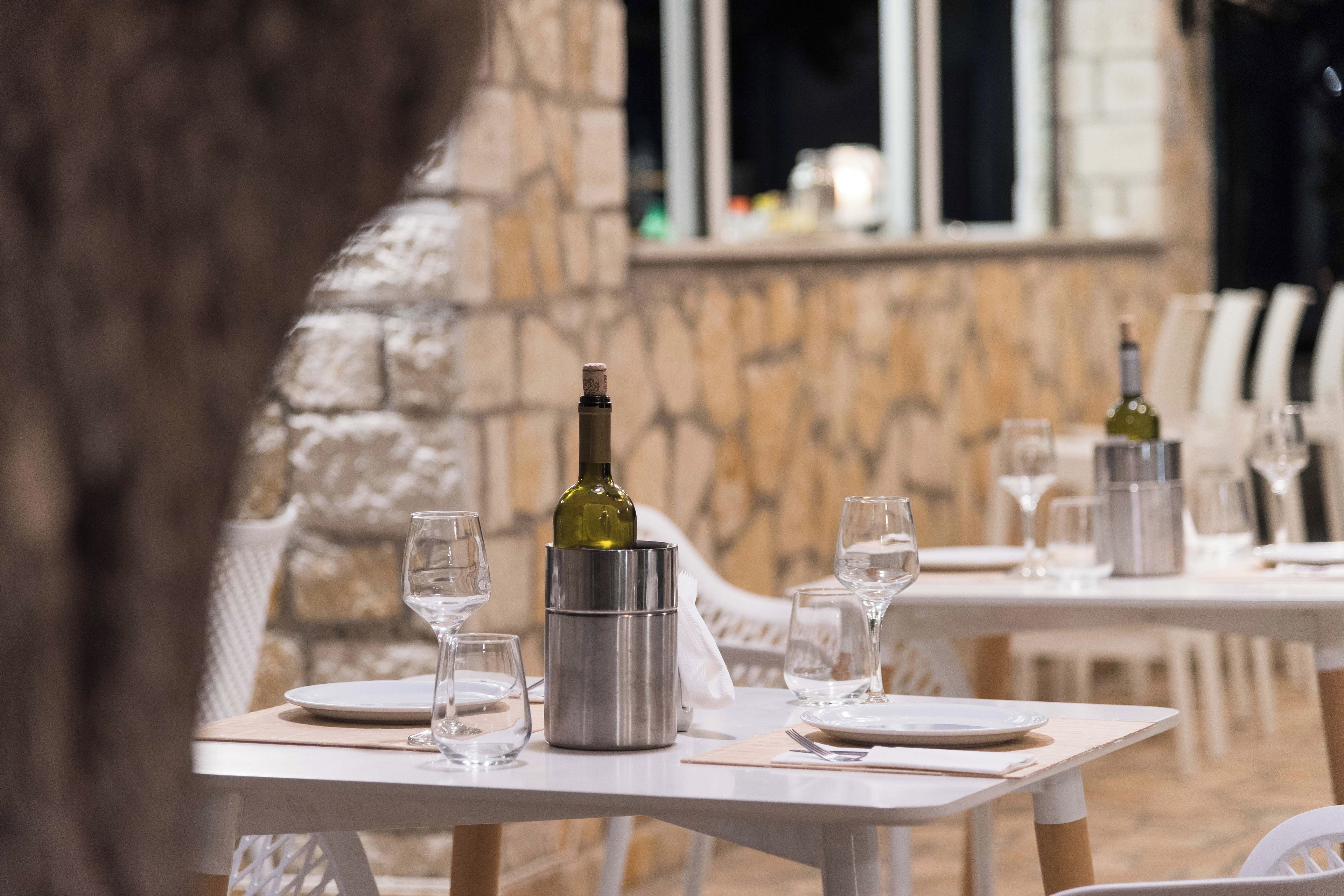 Un espace repas avec des tables préparées pour deux personnes, chacune agrémentée d’une bouteille de vin, de verres et de couverts.