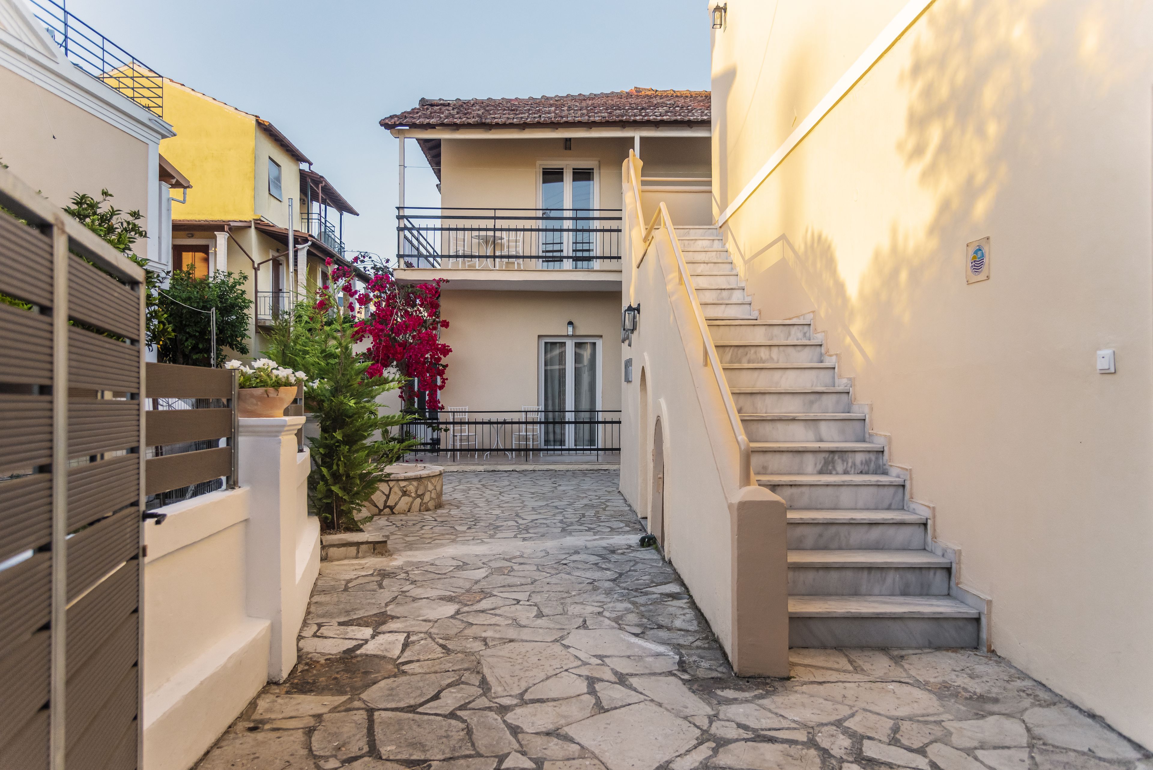 A narrow courtyard with a stone floor, a staircase on the right, and a building with a balcony on the left.