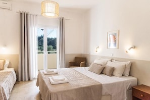 Ein Hotelzimmer mit Bett, Sessel, Tisch, einem Fenster mit Vorhängen und einer Wandleuchte.