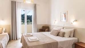 Habitación de hotel con cama, una silla, una mesa, ventana con cortinas y una lámpara fijada a la pared.