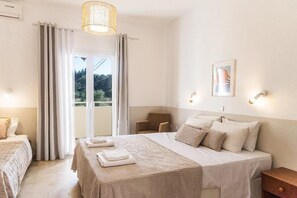 Ein Hotelzimmer mit Bett, Sessel, Tisch, einem Fenster mit Vorhängen und einer Wandleuchte.