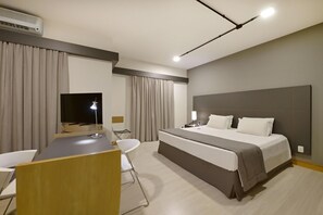 Ein Hotelzimmer mit Bett, Schreibtisch, Stuhl, Fernseher und Vorhängen.
