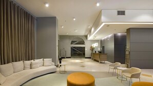 A modern interior with a curved sofa, a round ottoman, and a staircase leading to an upper level. - Araucária Plaza (Ribeirão Preto)