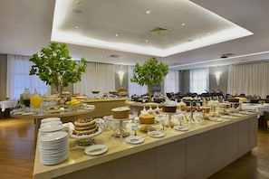 A buffet setup with various food items and a large plant in the center. - Araucária Plaza (Ribeirão Preto)