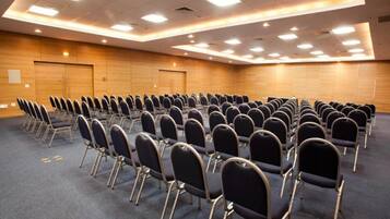 A conference room with rows of chairs, wooden walls, and ceiling lights.