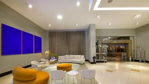 En moderne lobby med en buet sofa, hvide stole, en rund orange skammel og en glasklædt indgang.