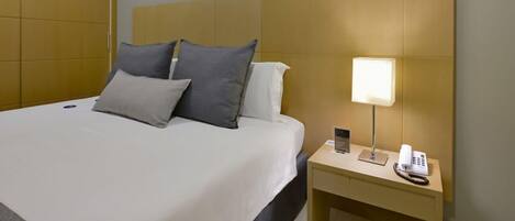 A hotel room with a bed, bedside lamp, phone, and a wooden headboard.