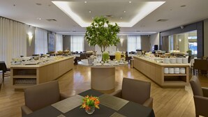 Et moderne hotelspisested med en central ø, forskellige siddepladser og en stor plante.