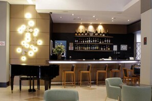 Zona de bar con piano, taburetes y una variedad de botellas.