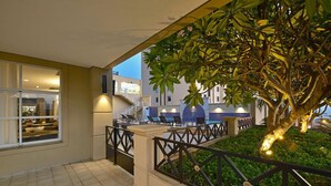 A poolside area with a tree, a railing, and a view of a building in the background. - Araucária Plaza (Ribeirão Preto)