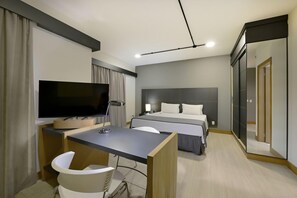 Une chambre d’hôtel comprenant un lit, un bureau avec une chaise, une télévision et un miroir.