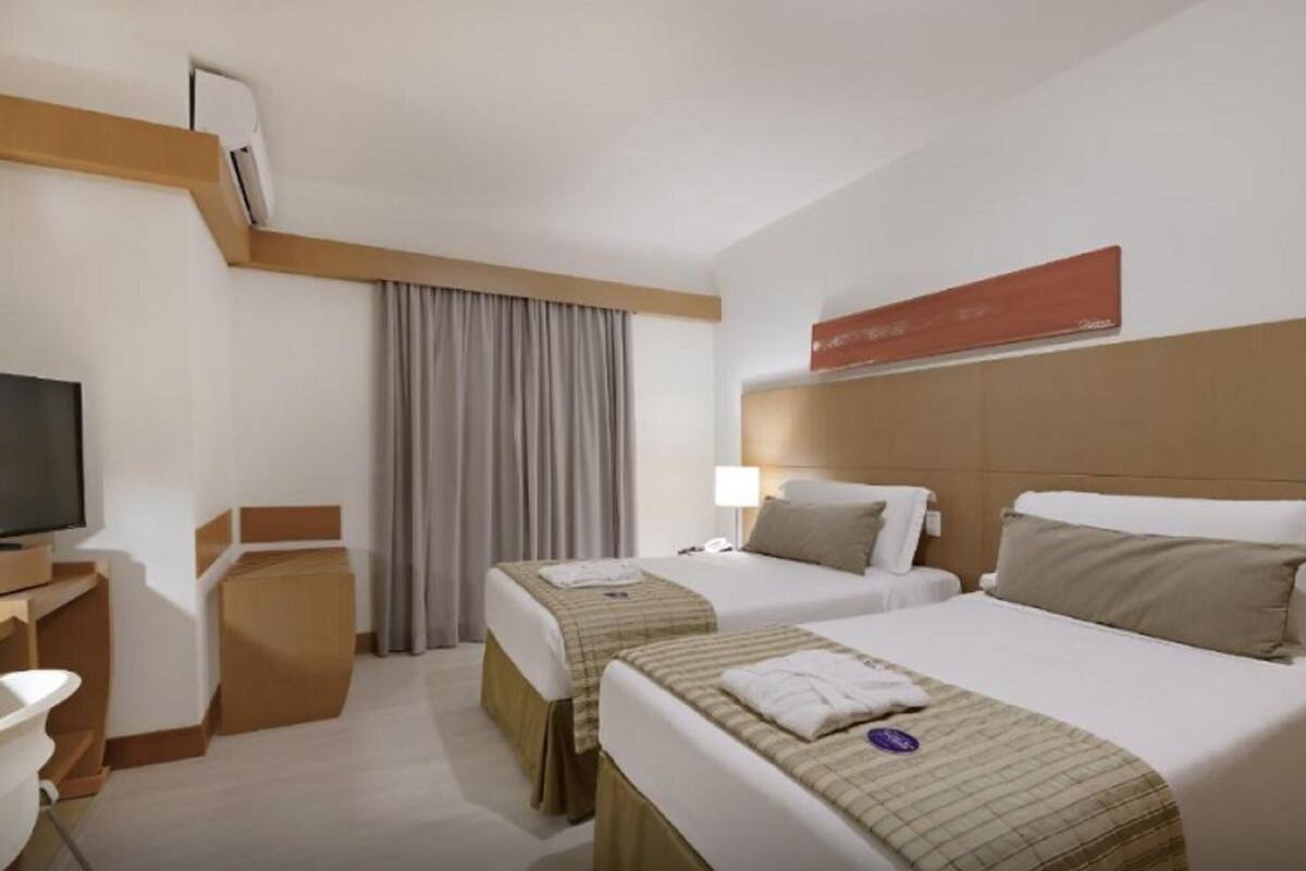Ein Hotelzimmer mit zwei Betten, einem Fernseher, einem Schreibtisch und einem Fenster mit Vorhängen.