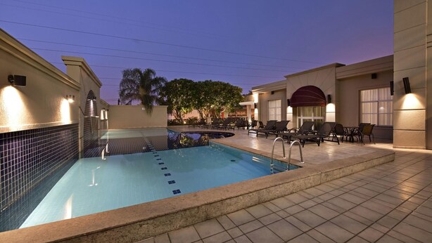 En swimmingpool med liggestole og en flisebelagt solterrasse.