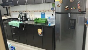 Ett kök med mörka skåp, ett kylskåp i rostfritt stål, en kaffebryggare och en vattenautomat.