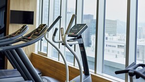 Ein Fitnessraum mit Laufbändern und Blick auf die Stadt durch große Fenster.