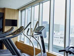 Et fitnesscenter med løbebånd og udsigt over byen gennem store vinduer.