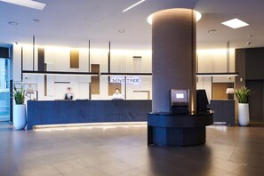 Et moderne hotelreceptionsområde med en receptionistskranke, en stor søjle, og en receptionistskranke med en skærm.