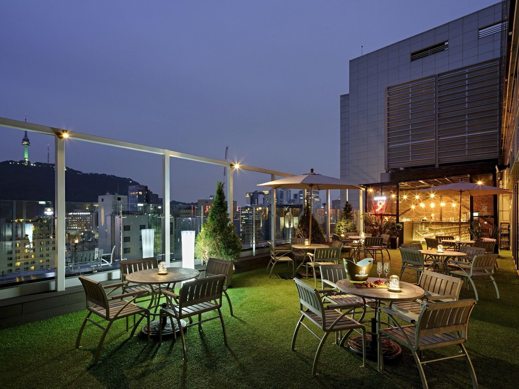 Eine Terrasse im Freien mit Tischen und Stühlen, einem Weihnachtsbaum und Blick auf die Stadt im Abenddämmerung.