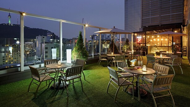 Eine Terrasse im Freien mit Tischen und Stühlen, einem Weihnachtsbaum und Blick auf die Stadt im Abenddämmerung.
