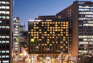 Et moderne hotel med et vinduesgitter, et tydeligt skilt der viser 'NINE TREE', og udsigt over det omkringliggende byområde.