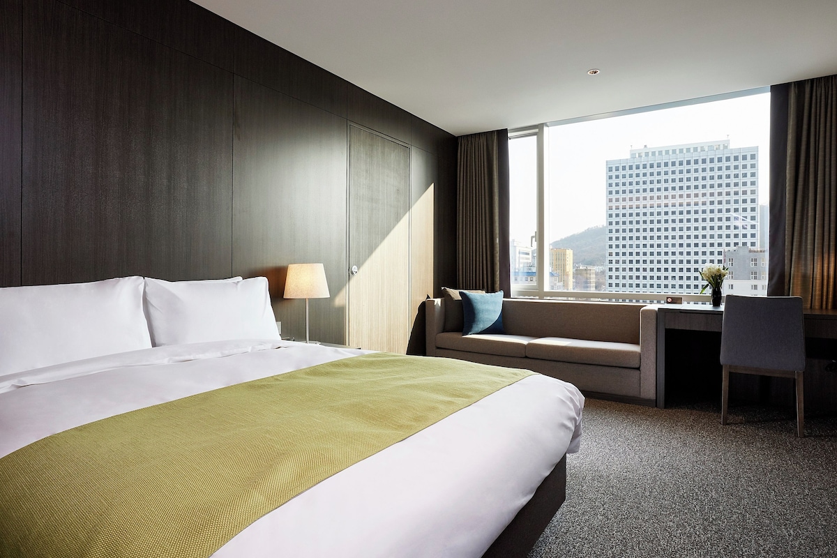 A hotel room with a large bed, a desk, and a view of a cityscape.